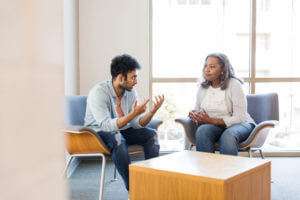 Young man gestures while sharing with female mental health counselor
