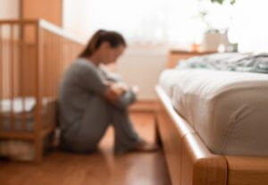 A mother with Postpartum Depression sitting on the floor next to a crib