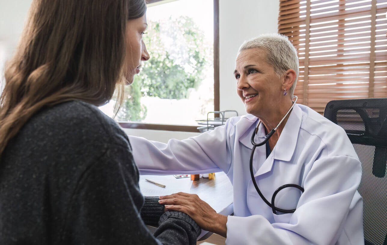 Elderly female doctor in white coat talking with a depressed young patient in clinic