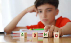 A blurred image of a frustrated child with attention deficit disorder doing homework while holding letters that spell ADHD.